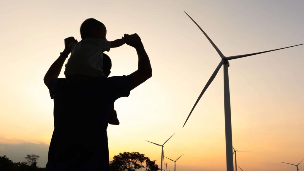 Vater mit Kind auf der Schulter vor Windrad in der Abendsonne